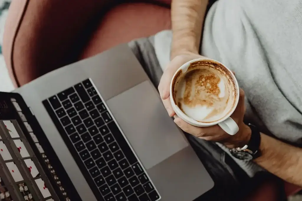 Person using a laptop while holding a cup of coffee