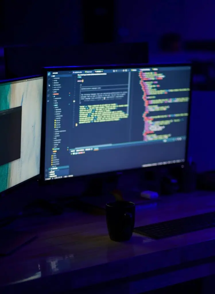 Computer monitors displaying software code in a technical workspace